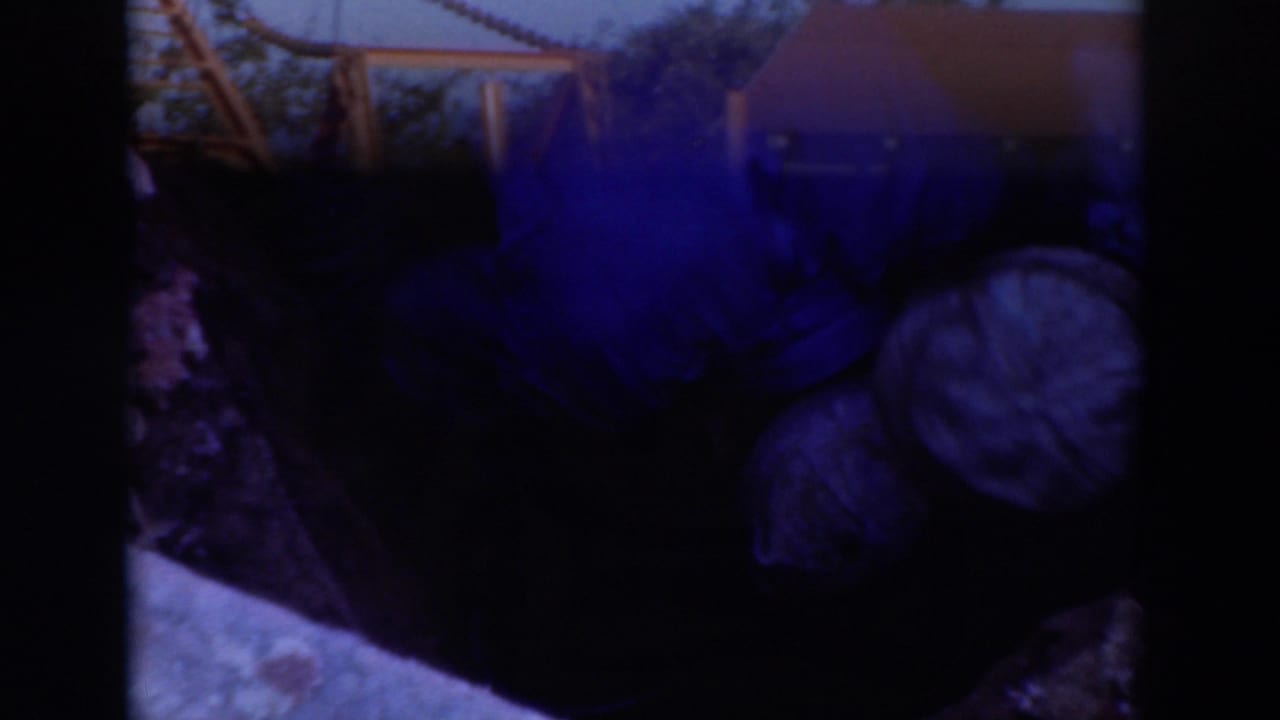 Sacramento 1937 home-movie frame looking down at two workers in caps crouched in a muddy trench near a pipe fitting.