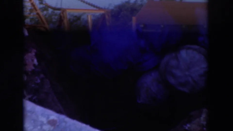 Sacramento 1937 home-movie frame looking down at two workers in caps crouched in a muddy trench near a pipe fitting.