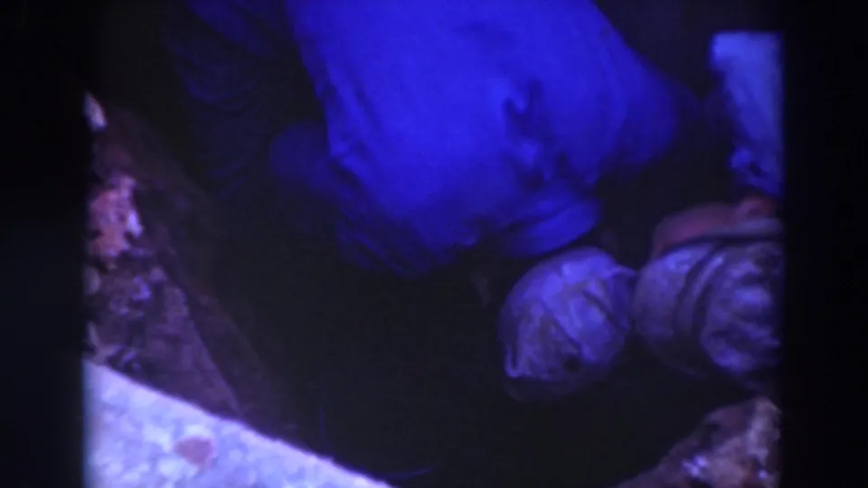 Blue-tinted 8mm frame of two Sacramento workers crouched close together in a muddy trench, one bent over the work area.