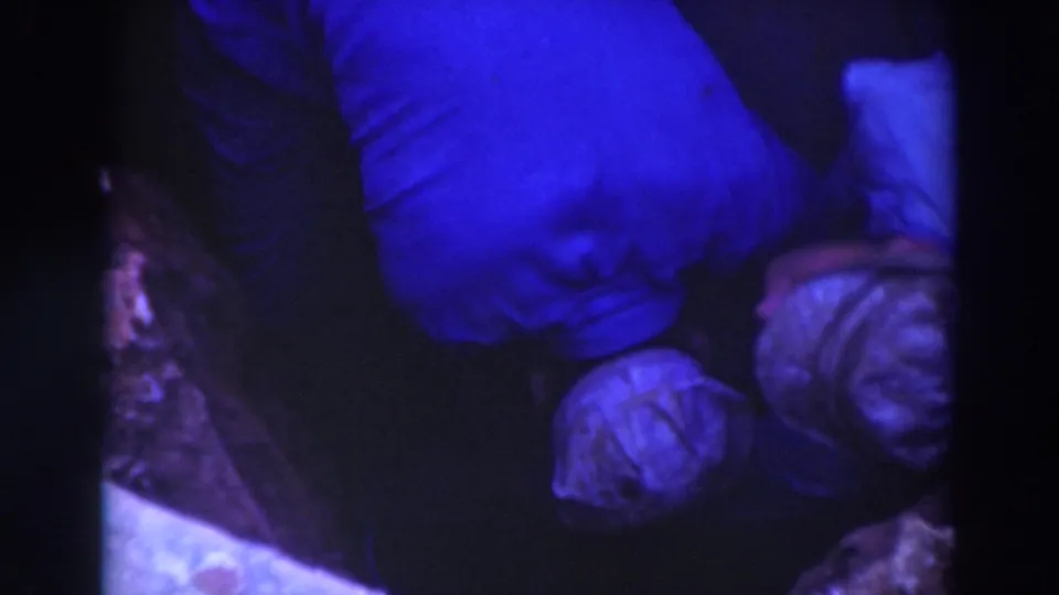 1937 Sacramento home-movie frame with workers clustered in a shadowed pit area, their pale hats standing out in blue-toned light.