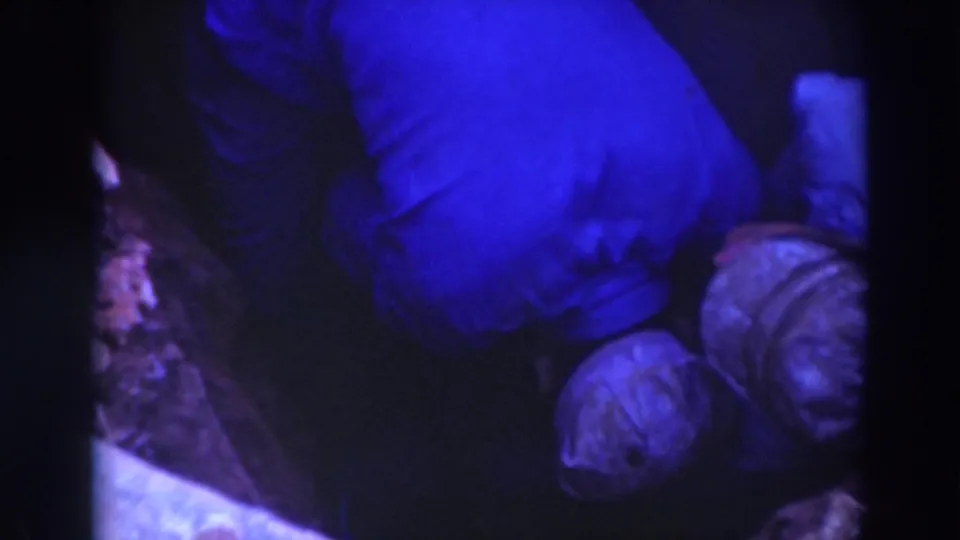 Sacramento 1937 home-movie frame showing capped men leaning into a cramped underground work area under dim blue-tinted light.