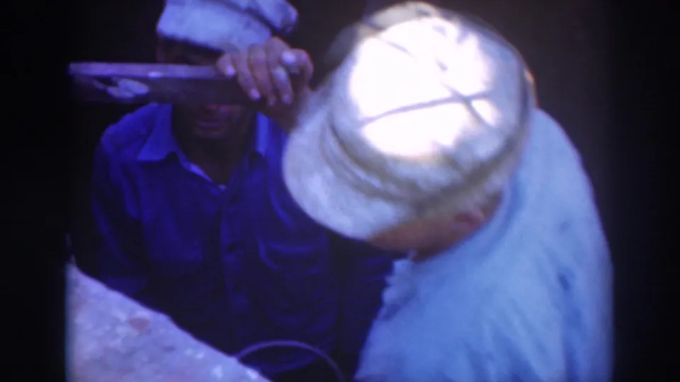 Sacramento 1937 frame with a man holding a shallow tray or pan beside another capped worker in a tight underground area.