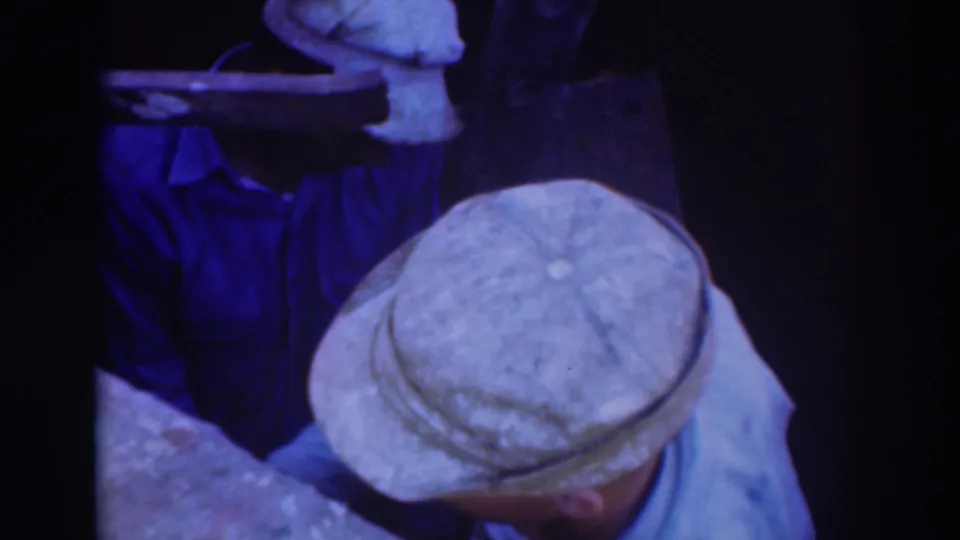 Sacramento 1937 frame showing a capped worker bending over a narrow underground area with another man partly visible behind him.