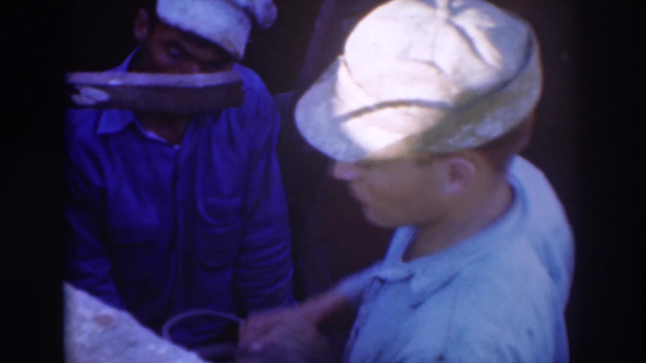 Two men in caps appear near the camera in 1937 Sacramento home-movie footage, one partly obscured by a light object across his face.