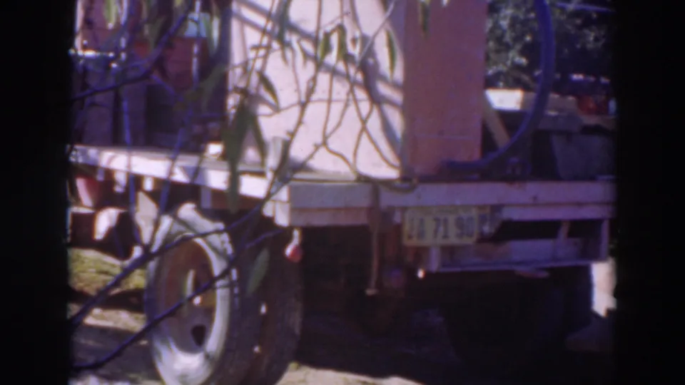 The final frame holds on the rear of the trailer, with branches in front and a grassy rural field around it.