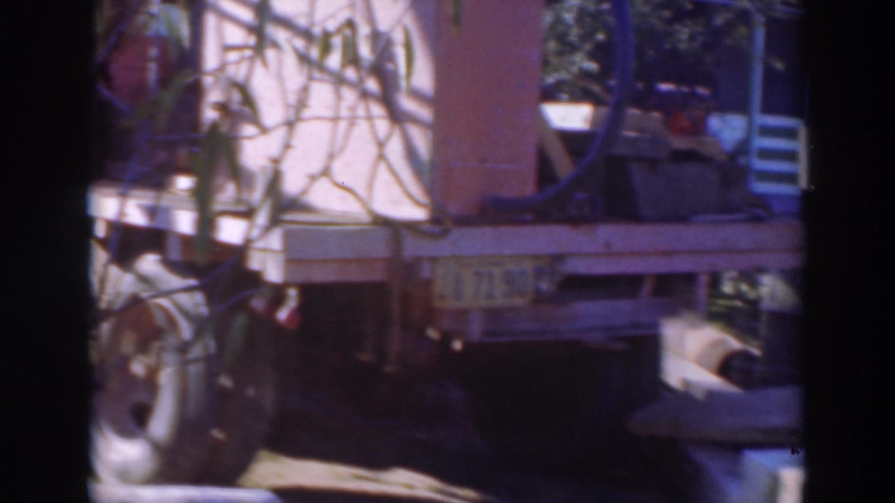 1937 Sacramento 8mm frame of a flatbed truck loaded with machinery, partly obscured by foliage and shadow.