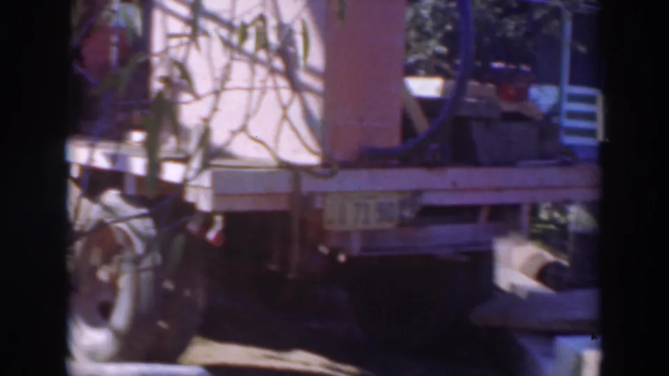 1937 Sacramento 8mm frame of a flatbed truck loaded with machinery, partly obscured by foliage and shadow.