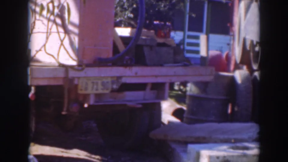 1937 Sacramento home-movie frame showing the rear of a flatbed truck, machinery, hoses, and metal barrels in a yard.