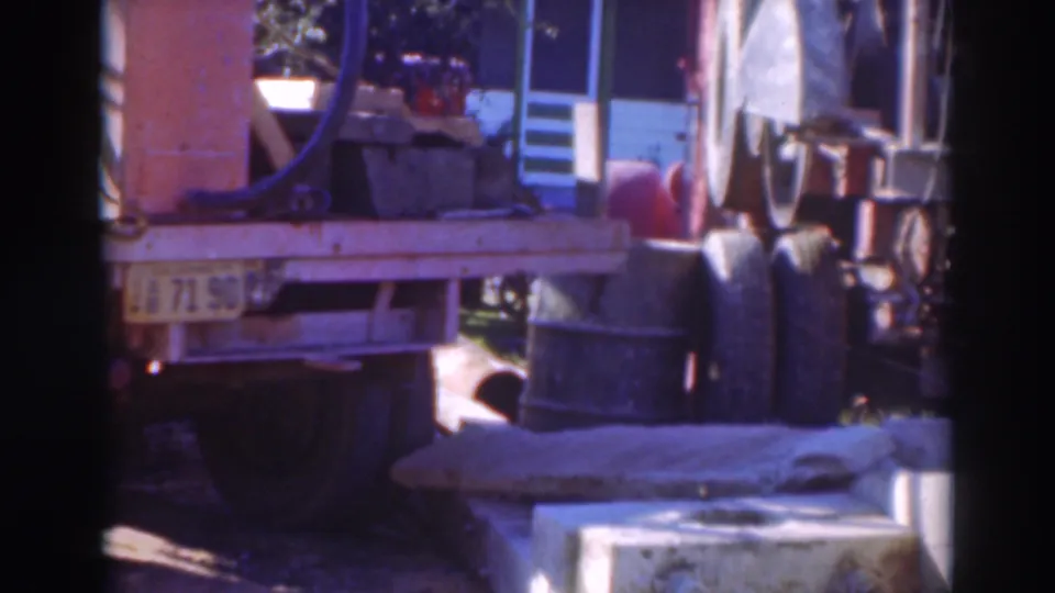 1937 Sacramento 8mm frame of a loaded truck with industrial equipment, barrels, and a low platform or curb in the foreground.