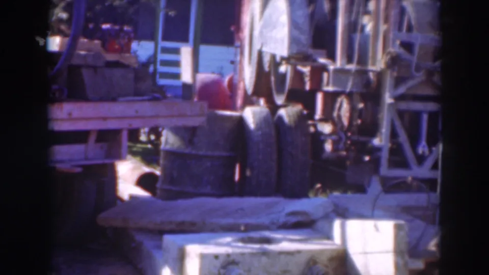 1937 Sacramento frame showing the side and rear of a flatbed truck with machinery, barrels, and structural rails nearby.
