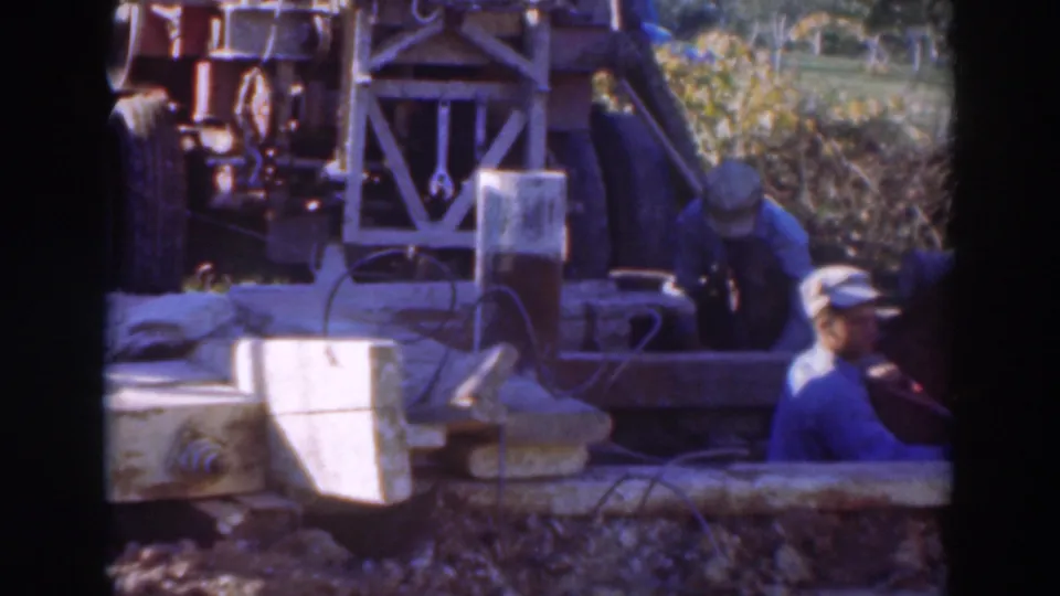 A Sacramento construction worker in a blue shirt stands beside a trench, with drilling equipment and cables visible behind him.