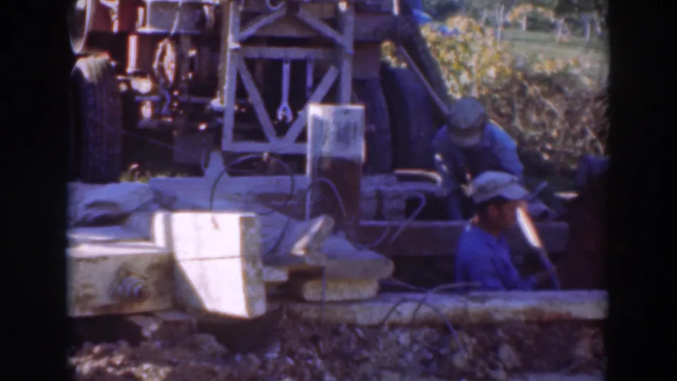Workers at a 1937 Sacramento trench site remain focused on excavation work around a drilling rig, cables, and rough ground.