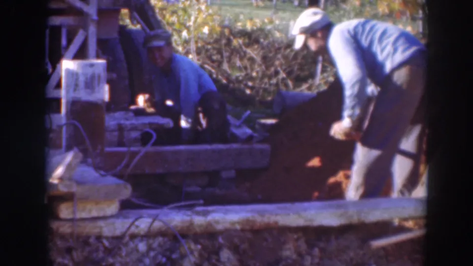 A man in a cap shovels near exposed earth while another man remains seated by tools in the Sacramento work scene.