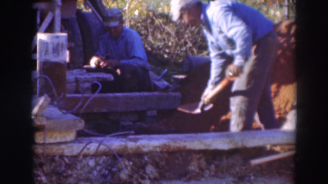 1937 Sacramento 8mm frame showing a seated worker with a small tool and another worker bending over a shovel at a rough outdoor worksite.