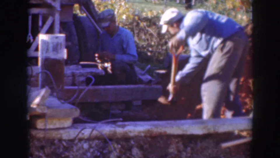 1937 Sacramento 8mm still with a foreground worker using a shovel and a seated worker behind him near planks, soil, and worksite equipment.