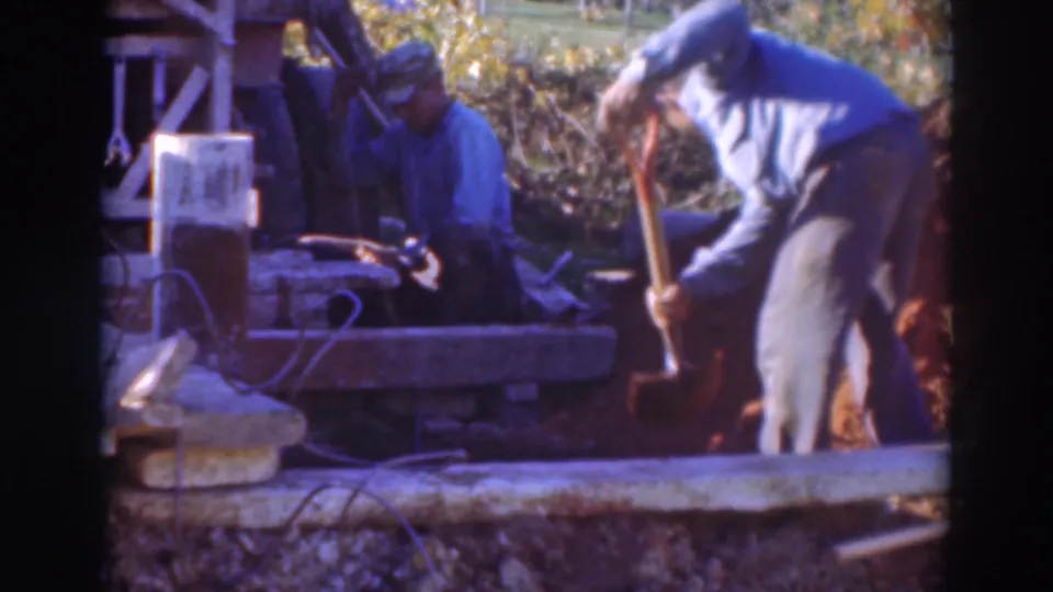 A Sacramento worksite scene shows one capped man digging while another remains seated beside equipment in 1937 home-movie footage.