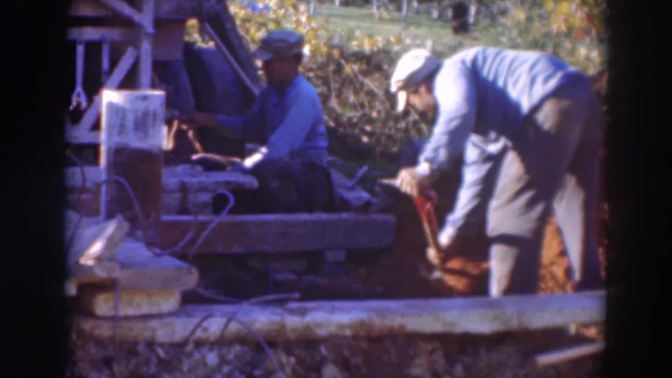 Two capped men work beside concrete blocks and loose soil, with one handling equipment and the other digging at the Sacramento site.