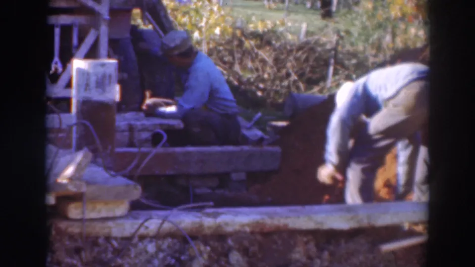 The 1937 Sacramento frame shows one man seated near a wooden structure as another bends over the work area with a tool.