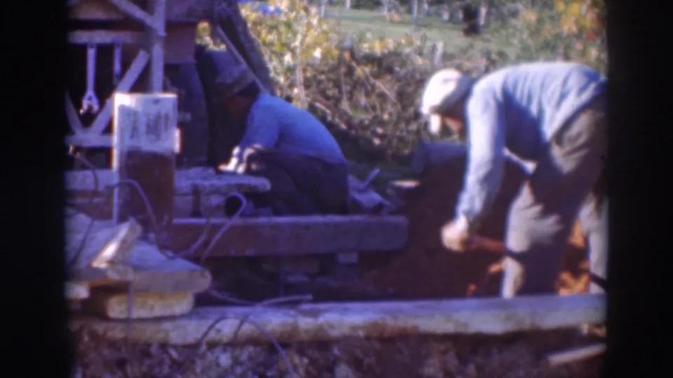 Sacramento 1937 construction scene with a man shoveling in the foreground and another worker kneeling near equipment by a foundation.
