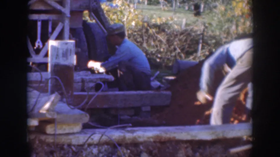 Outdoor 1937 Sacramento construction footage showing a kneeling man at equipment and another worker bent over near loose earth.