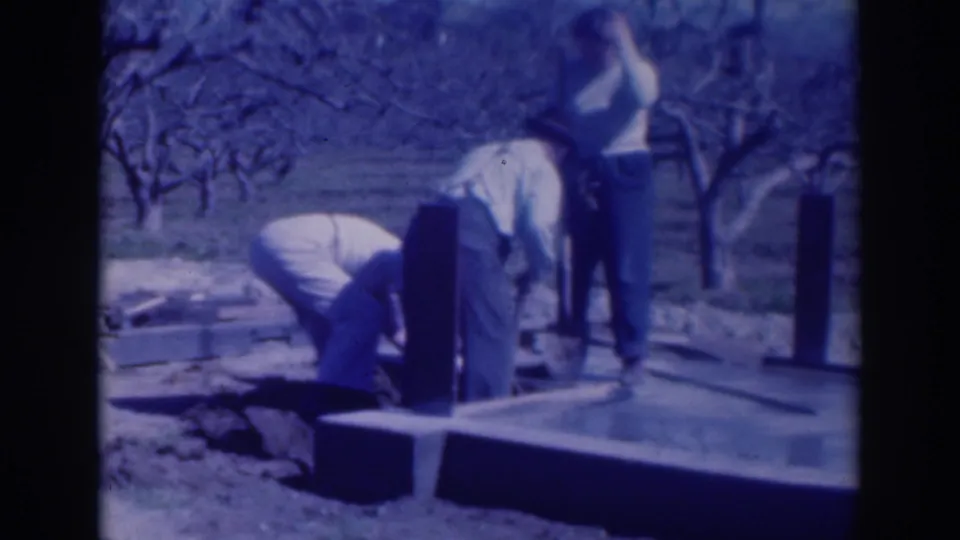 Three adults are seen beside upright posts and a concrete platform, with leafless orchard rows behind them in Sacramento.