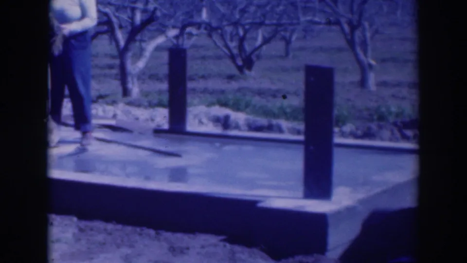 Late frame of the 1937 Sacramento home movie, focused on the wet foundation, upright posts, and orchard background.