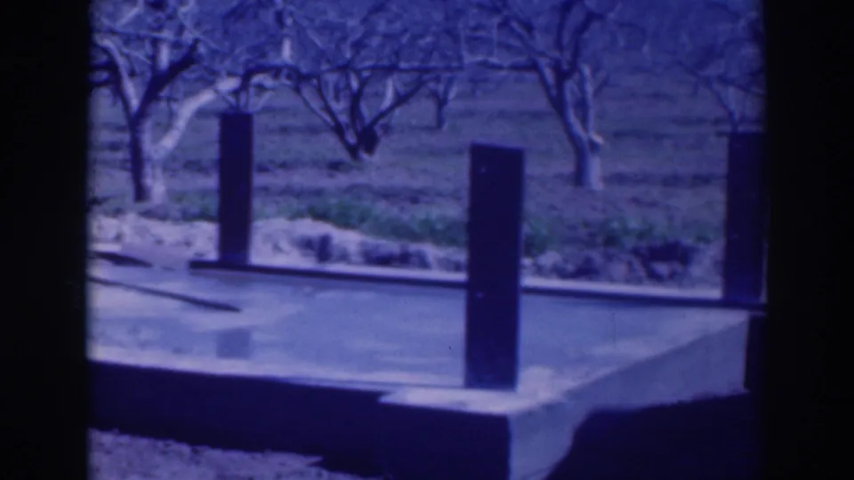 1937 Sacramento frame of a small concrete platform and upright posts set against bare orchard trees and low grass.
