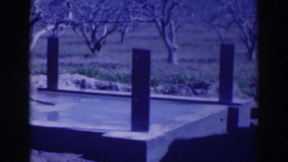 1937 Sacramento 8mm view of the platform, dark vertical posts, bare orchard trees, and surrounding field.