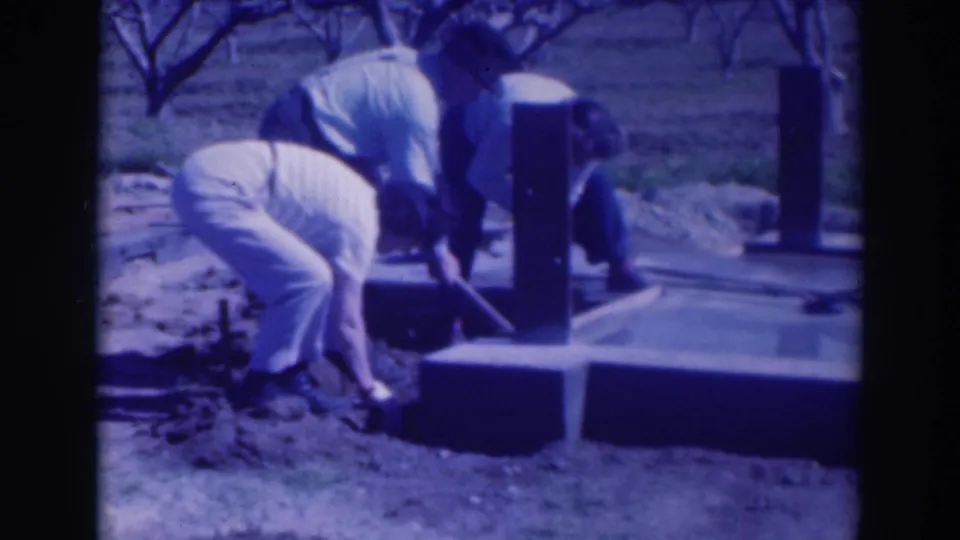 1937 Sacramento home-movie frame showing a man bending near a concrete platform and posts, with another figure partly visible nearby.