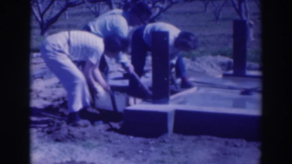 In 1937 Sacramento home-movie footage, two adults dig beside a concrete foundation with bare orchard trees behind them.