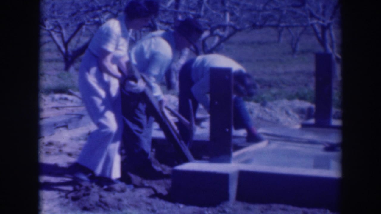 Three adults work around a wooden beam and concrete base outdoors.