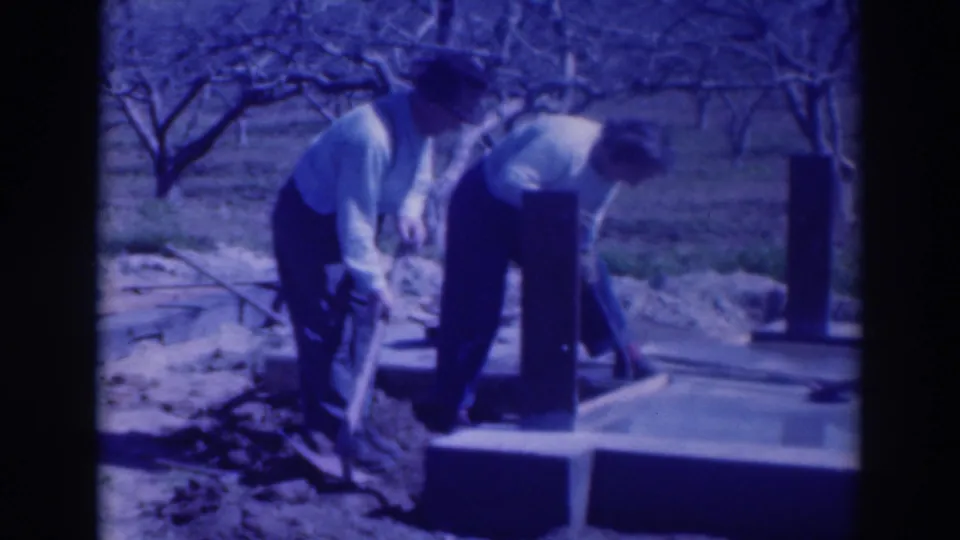 Two adults continue digging or handling material beside a concrete base in 1937 Sacramento outdoor home-movie footage.