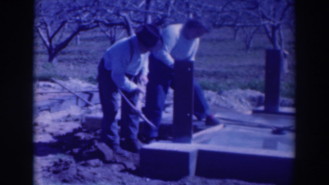 In supplied 1937 Sacramento footage, two men work over a concrete footing or foundation among bare orchard trees.