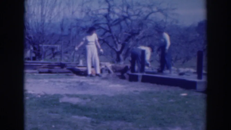 1937 Sacramento frame with two adults near scattered boards or blocks on a grassy lawn beneath leafless trees.