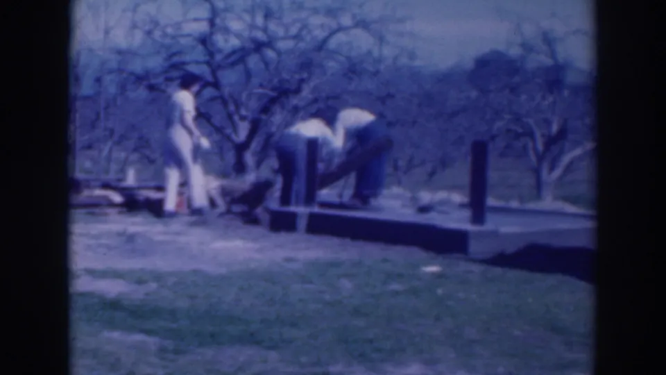 Adults in a Sacramento yard handle long materials near a small raised platform with bare trees behind them.