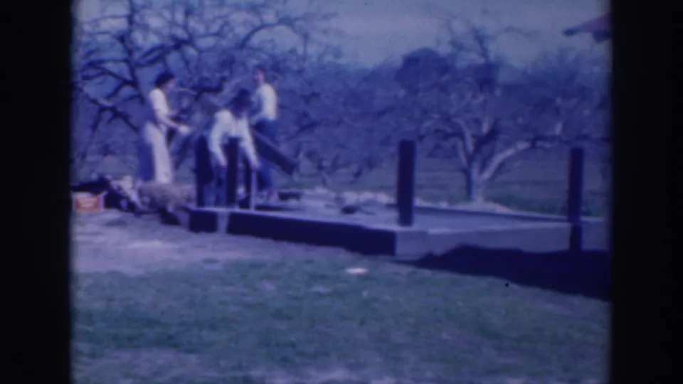 1937 home-movie frame from Sacramento showing three adults working around a platform with posts and scattered materials.
