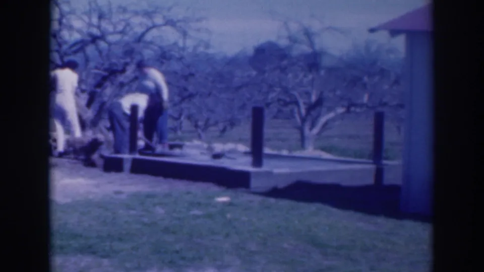 Adults in a 1937 Sacramento yard bend and stand around a low platform, with posts, grass, and leafless trees visible.