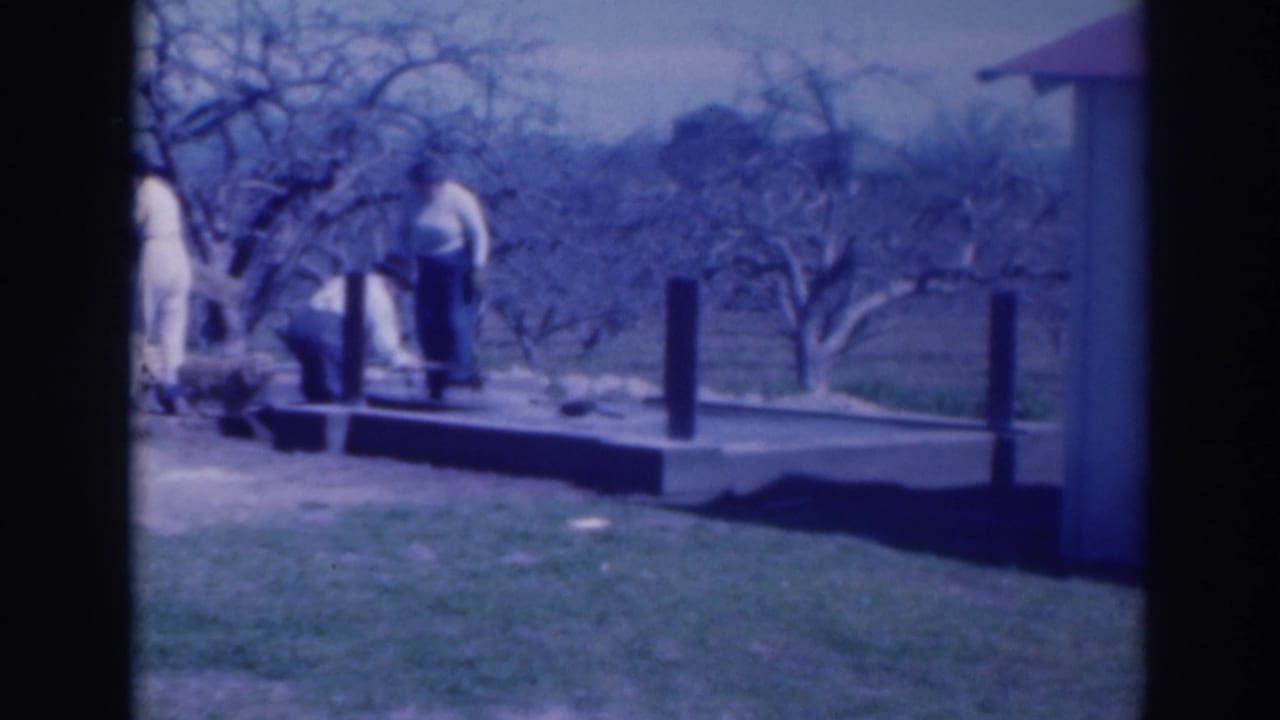 Adults stand near a small outdoor platform beside grass and bare trees.