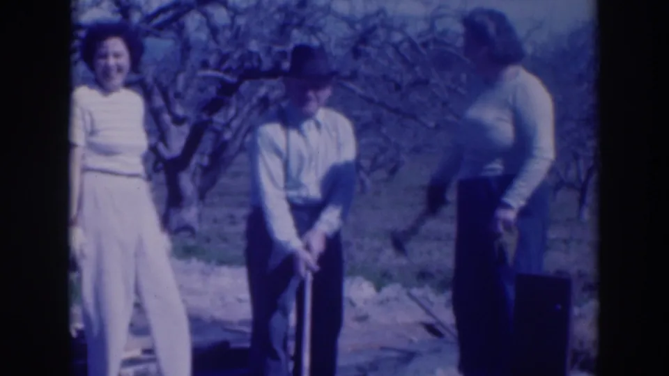 In this 1937 Sacramento home-movie frame, a man with a hat works a garden tool as two women stand beside him in a bare-tree yard.