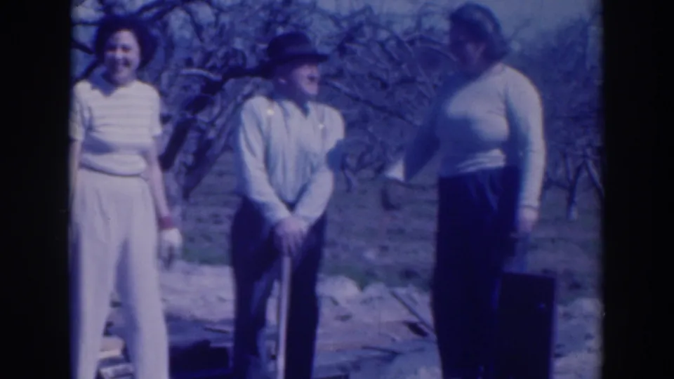 A 1937 Sacramento home-movie frame shows three adults smiling and interacting in a leafless garden or orchard setting.