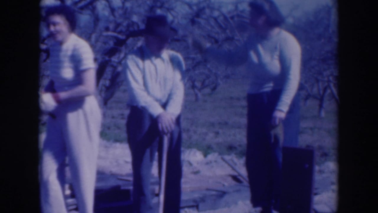 A woman smiles near an older man while another woman looks down beside a dark case.