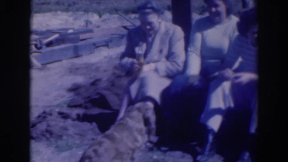 Adults sit or crouch near disturbed ground while a dog stands in the foreground in the supplied 1937 Sacramento home-movie scene.