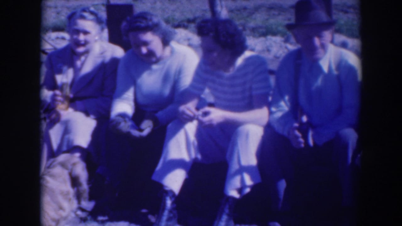 Four adults sit close together outdoors, with a dog partly visible.