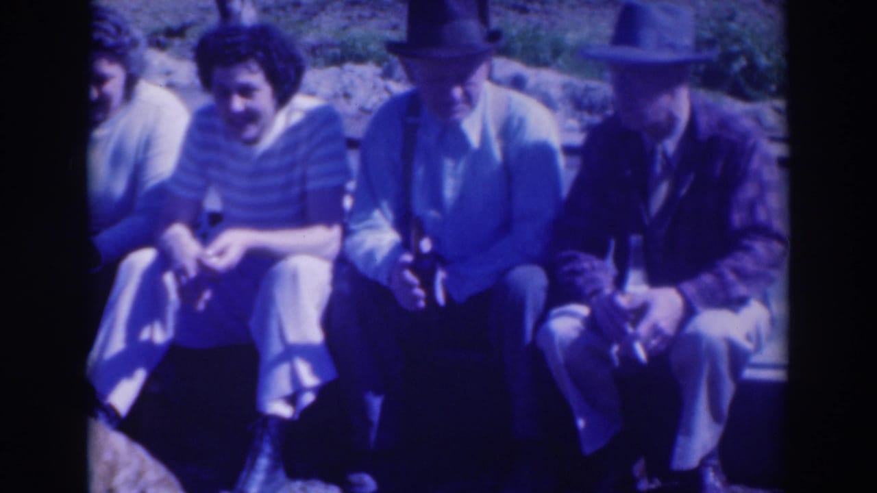 Four adults sit outdoors, with two men in hats and a woman in a striped top visible.