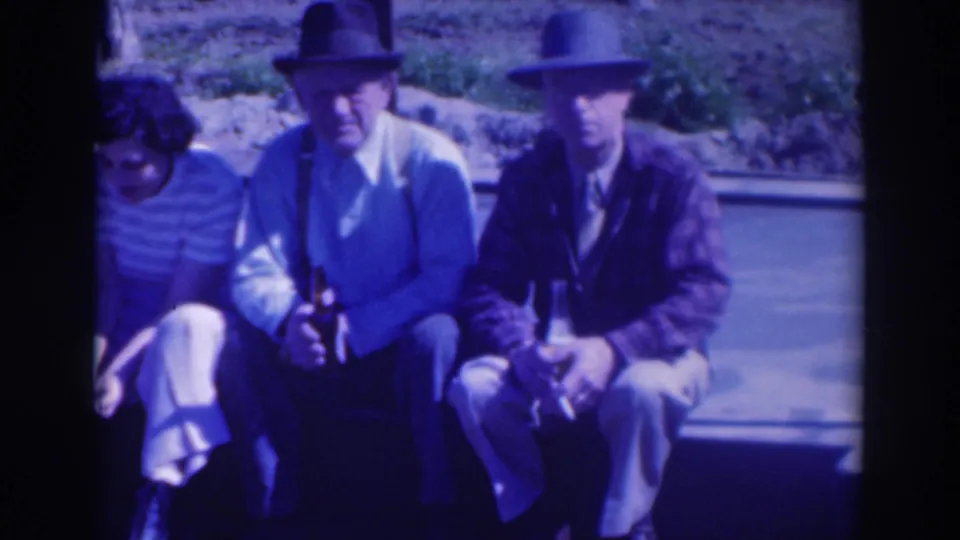 Two men in 1930s-style hats sit outdoors in Sacramento, with a woman partly visible at the left edge of the home-movie frame.