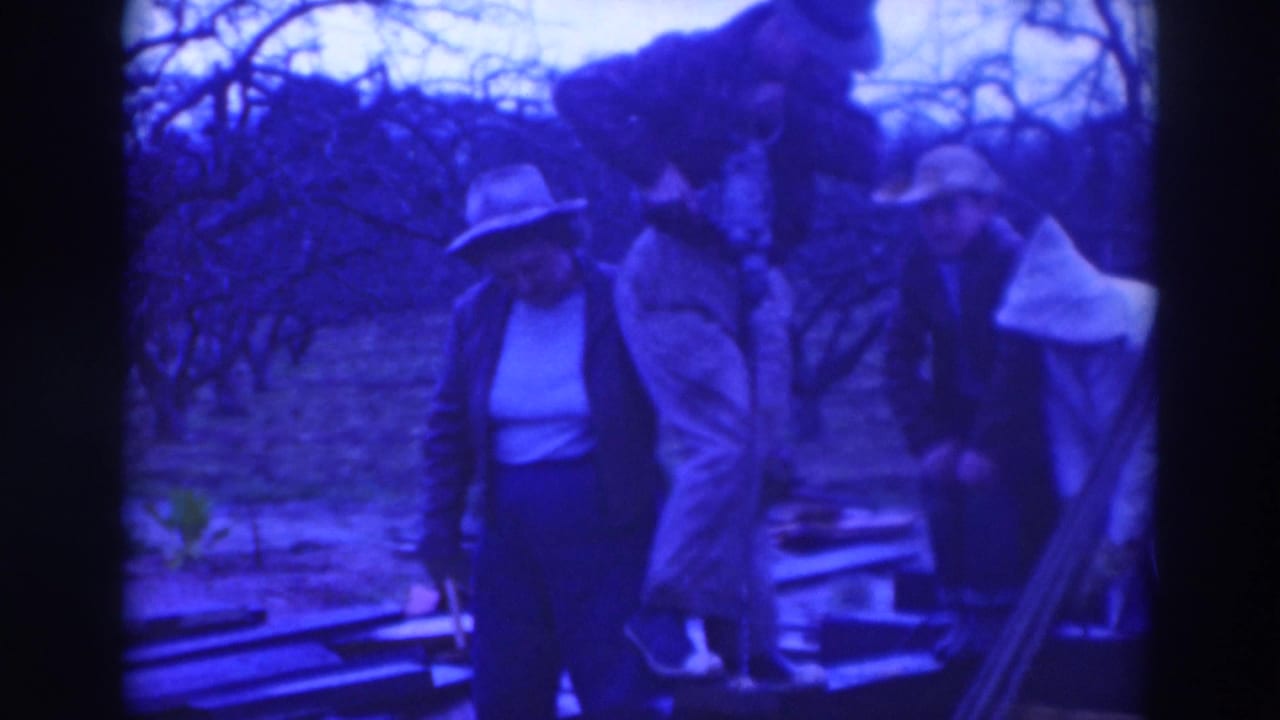 Several adults in hats and coats stand beside a pit or work area outdoors.