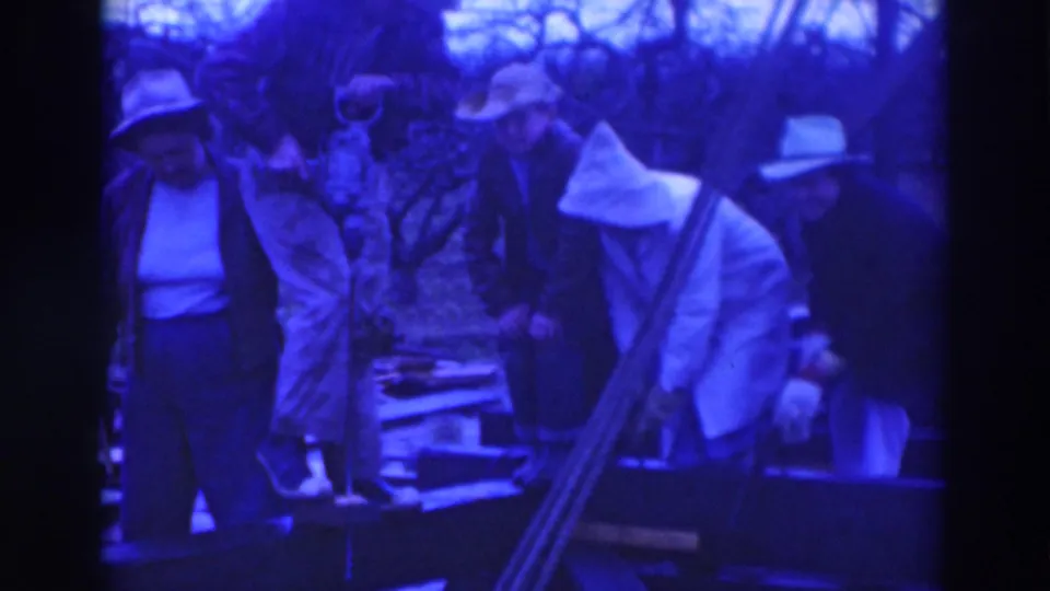 Blue-toned 8mm frame of adults in 1937 Sacramento watching work near a pit, with rails and bare trees behind them.