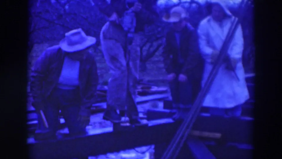 Late-1930s Sacramento construction frame showing men beside wooden house framing in soft, blue-shifted 8mm footage.