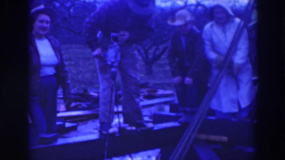 A woman at left and several adults in Sacramento stand near a wooden work area, with a tool and boards visible in the foreground.
