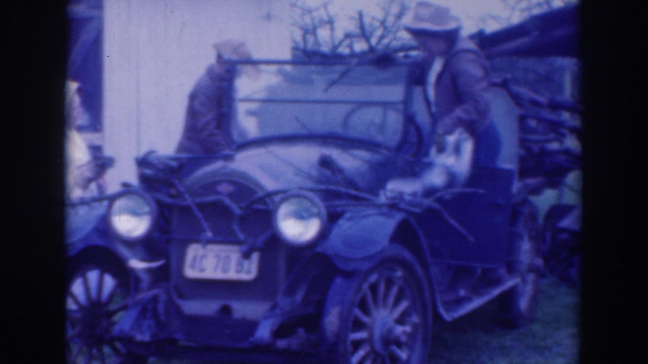 In 1937 Sacramento home-movie footage, two adult men stand beside an open vintage car with round headlights and a visible California plate.
